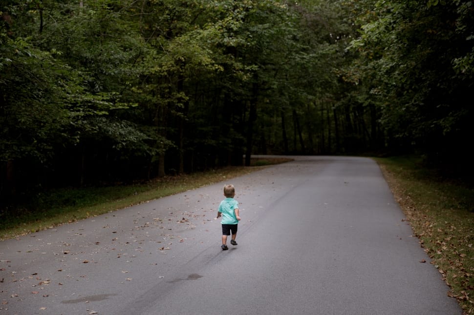 boy wearing teal shirt and black short walking in the black asphalt road preview