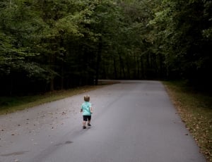 boy wearing teal shirt and black short walking in the black asphalt road thumbnail