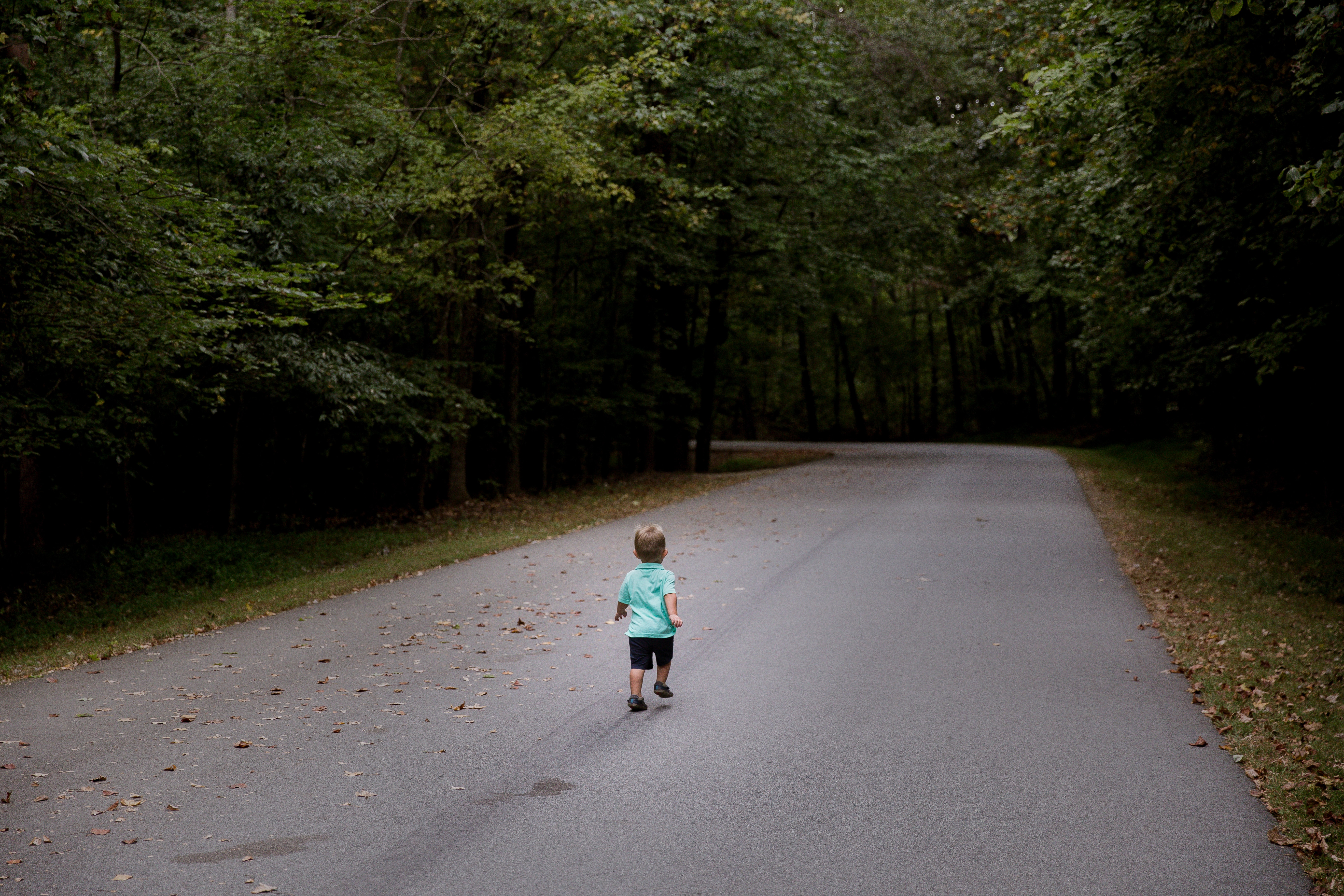 boy wearing teal shirt and black short walking in the black asphalt road