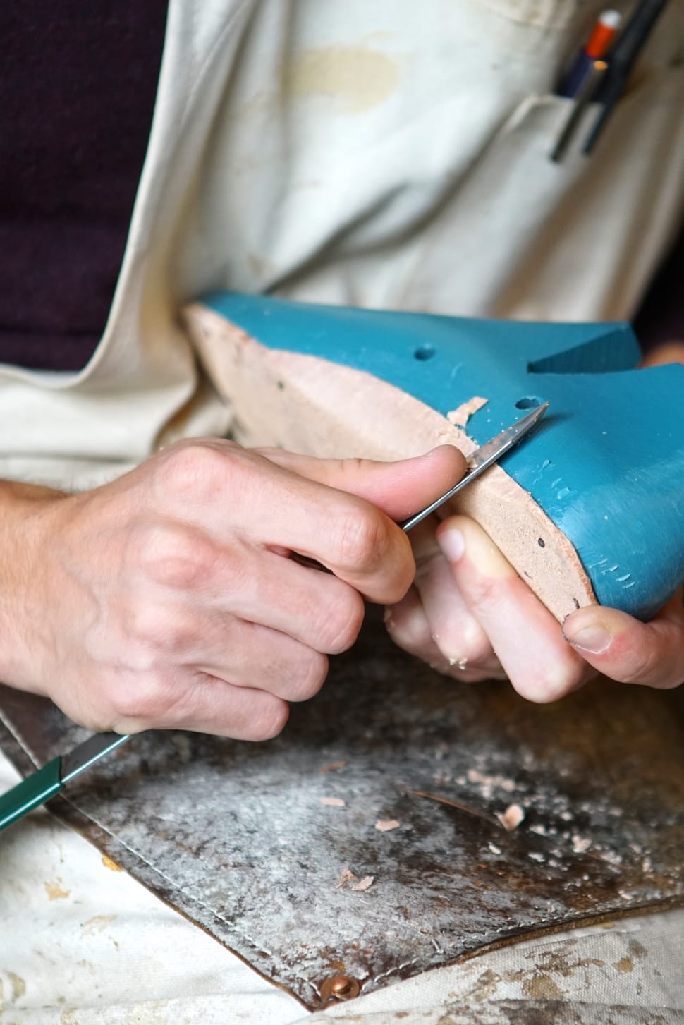 person holding gray knife while cutting blue and brown wooden shoe preview