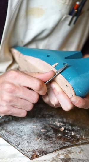 person holding gray knife while cutting blue and brown wooden shoe thumbnail