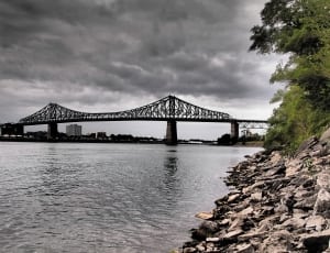 gray bridge above body of water under gray clouds during daytime photo thumbnail