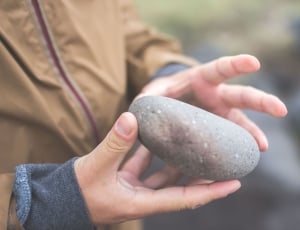 human holding round gray stone thumbnail