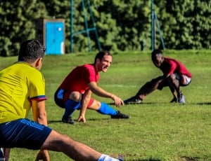 three men with soccer uniform doing leg bend on green grass filed thumbnail