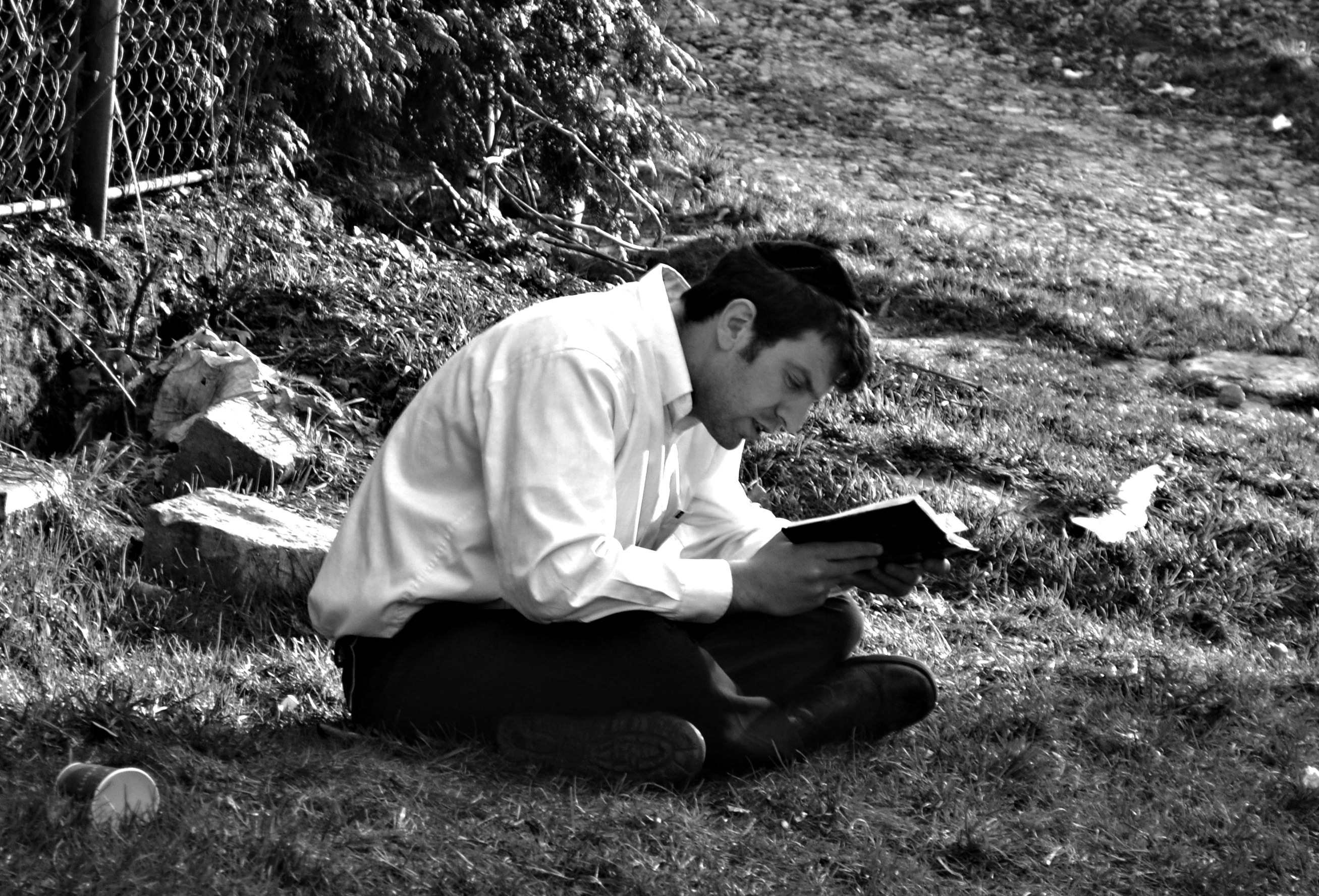 grayscale photo of man reading a book while sitting on grass