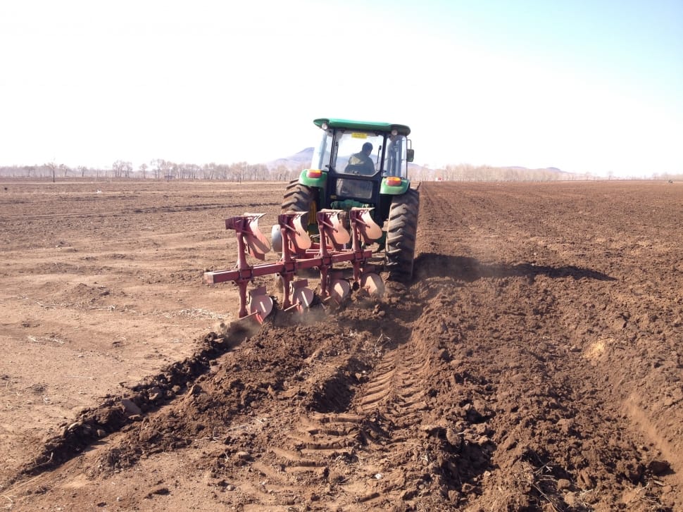 man driving green tractor with disk harrow on dirt field during daytime preview