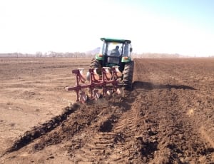 man driving green tractor with disk harrow on dirt field during daytime thumbnail