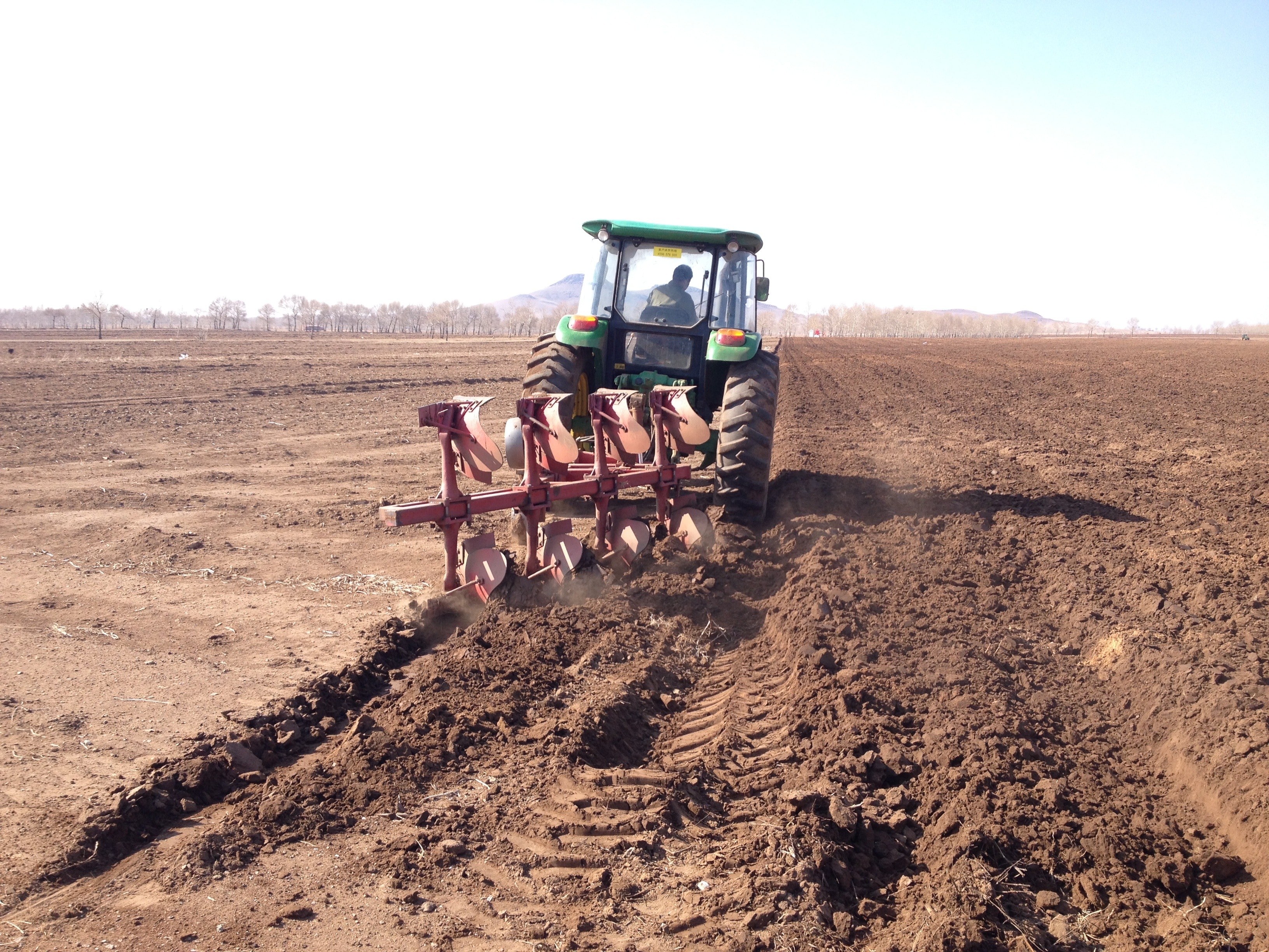 man driving green tractor with disk harrow on dirt field during daytime