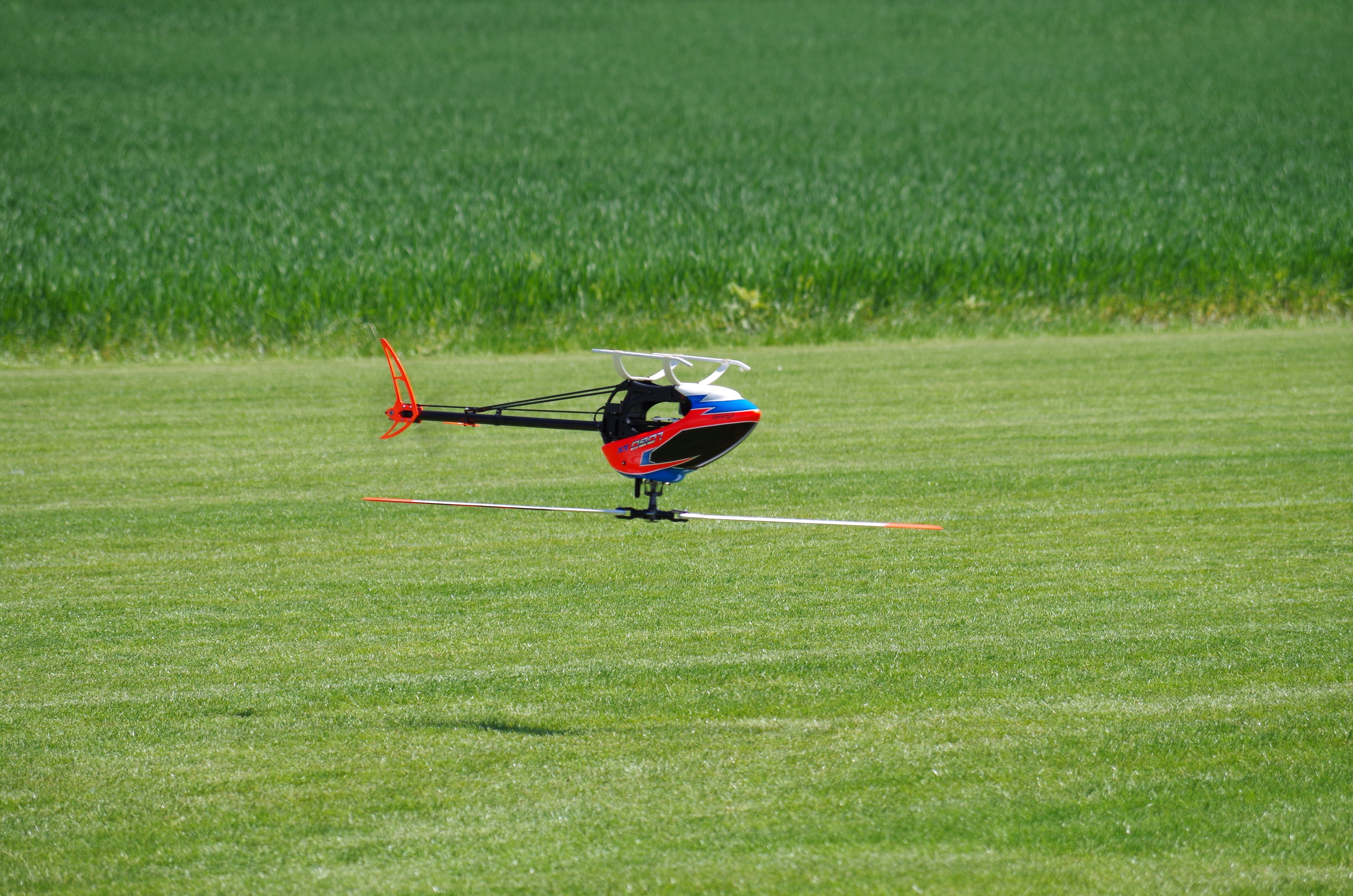 red, black and blue rc helicopter flying above green grass field during daytime