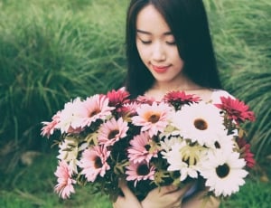 woman holding white, pink and red flowers on grass field during daytime thumbnail