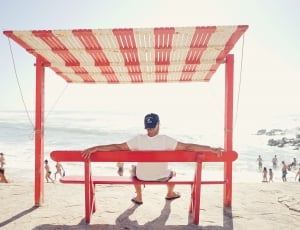 man wearing white t shirt seating on bench near shoreline thumbnail