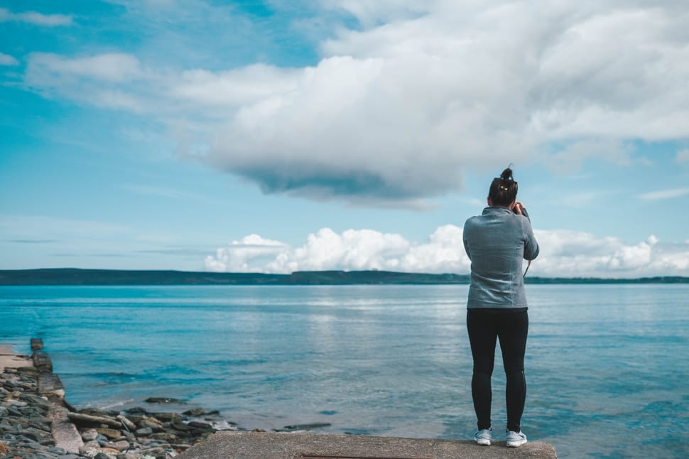 woman in black skinny pants using dslr camera near ocean during daytime preview