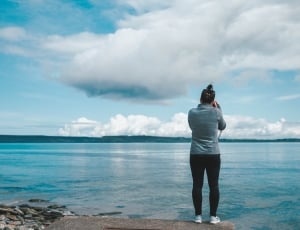woman in black skinny pants using dslr camera near ocean during daytime thumbnail