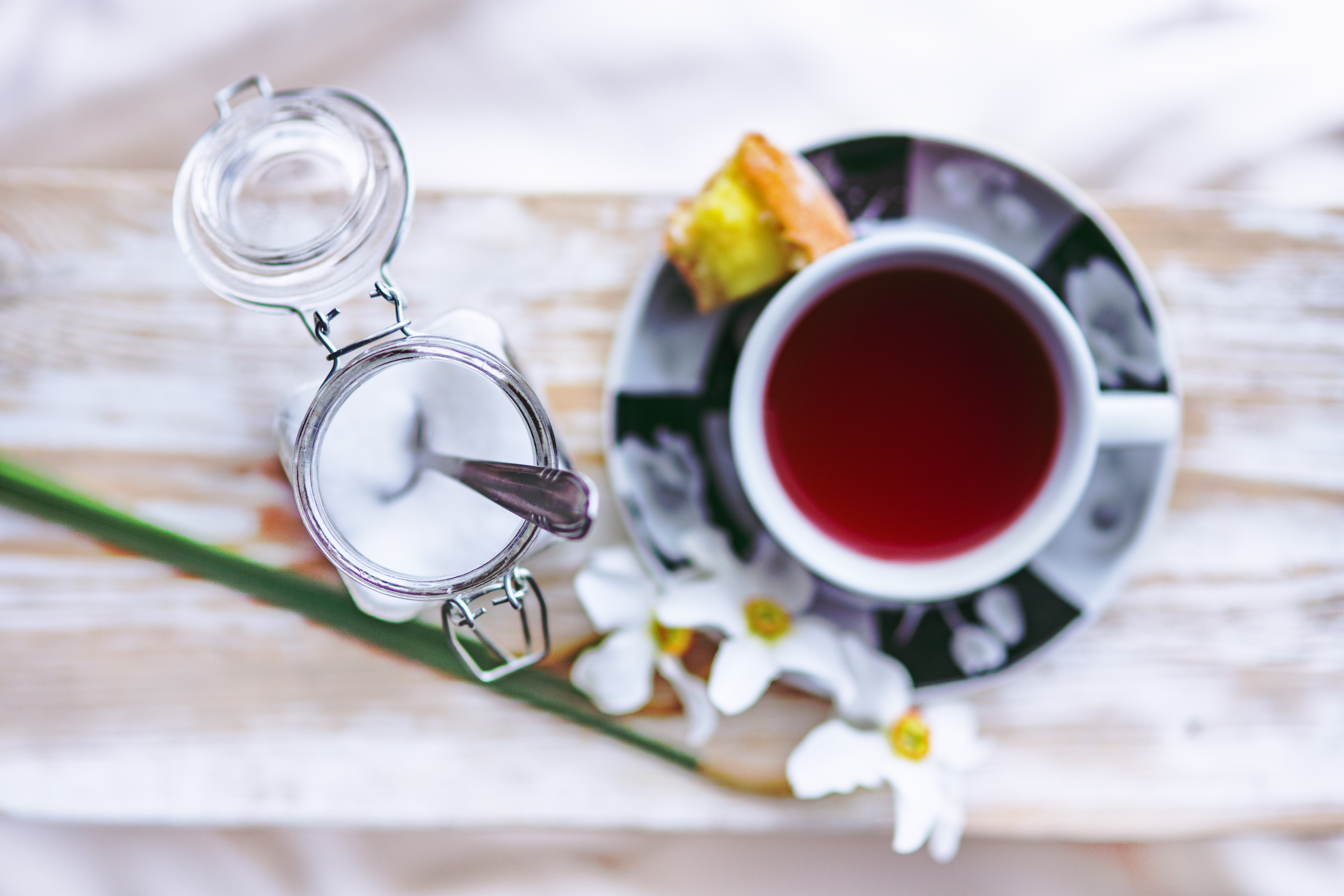shallow focus photography of sugar with spoon and red liquid filled white mug