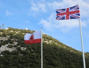 two flags near green grassy mountain during daytime thumbnail