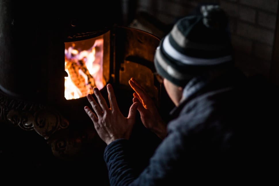 shallow focus photography of person in black jacket sitting in front of black furnace preview