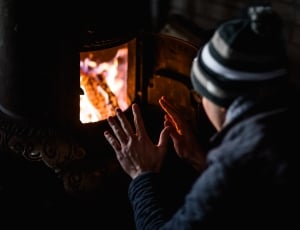 shallow focus photography of person in black jacket sitting in front of black furnace thumbnail
