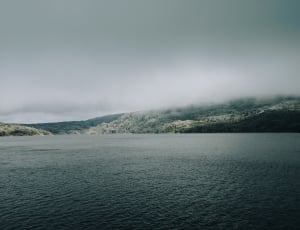 body of water and mountain under gray sky thumbnail