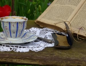 white and blue ceramic teacup set, brass framed bifocals and white knit doily thumbnail