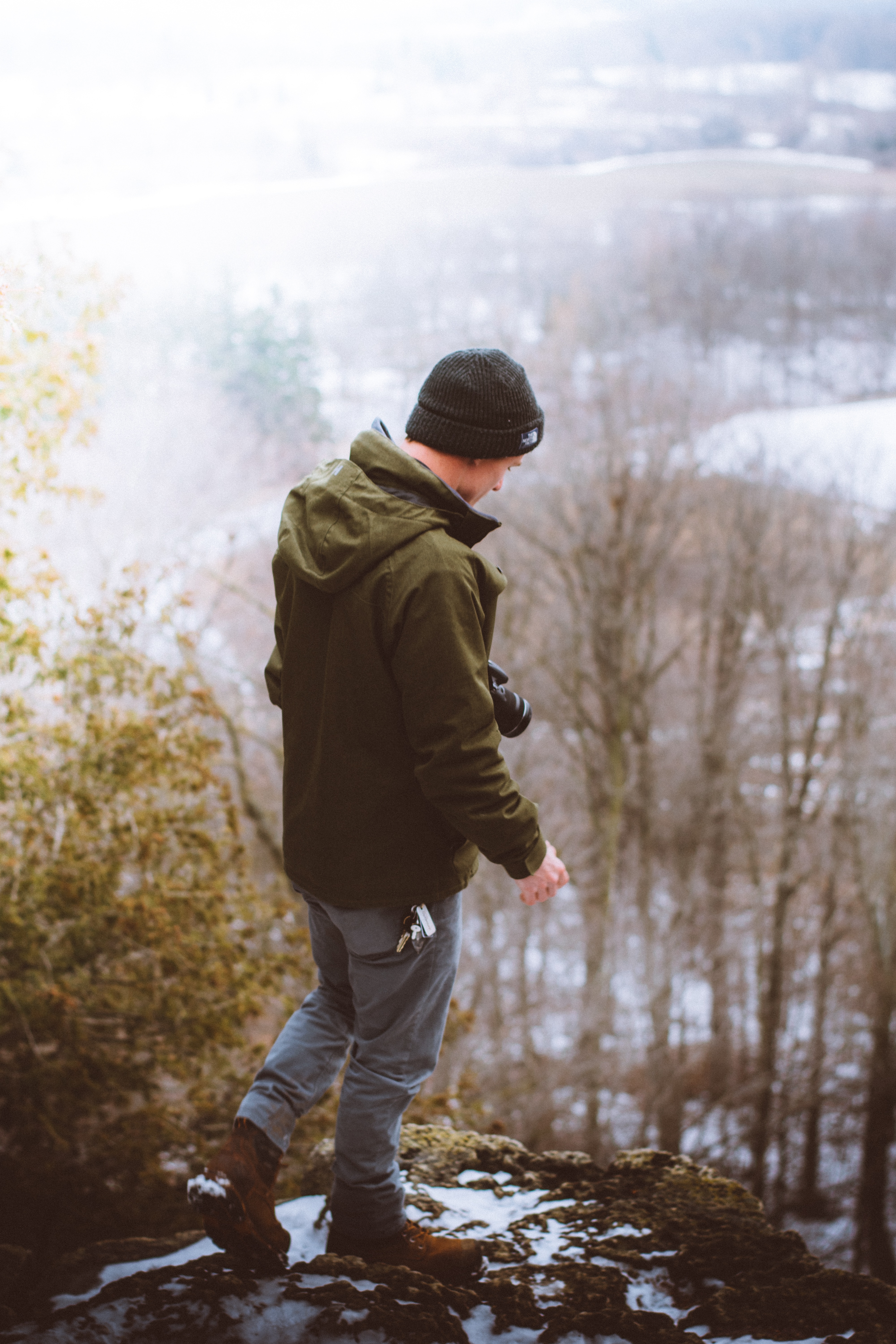man in green full zip hoodie standing on rocks near trees and mountain