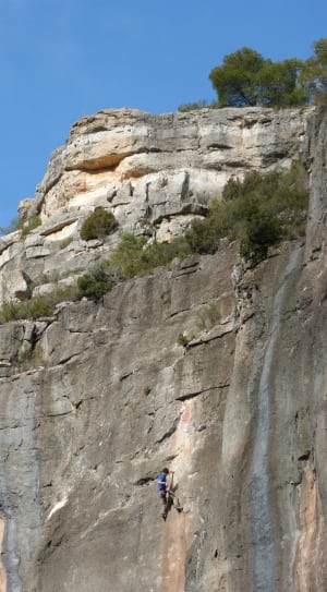 man wearing blue t-shirt climbing on rocky mountain under clear blue sky thumbnail