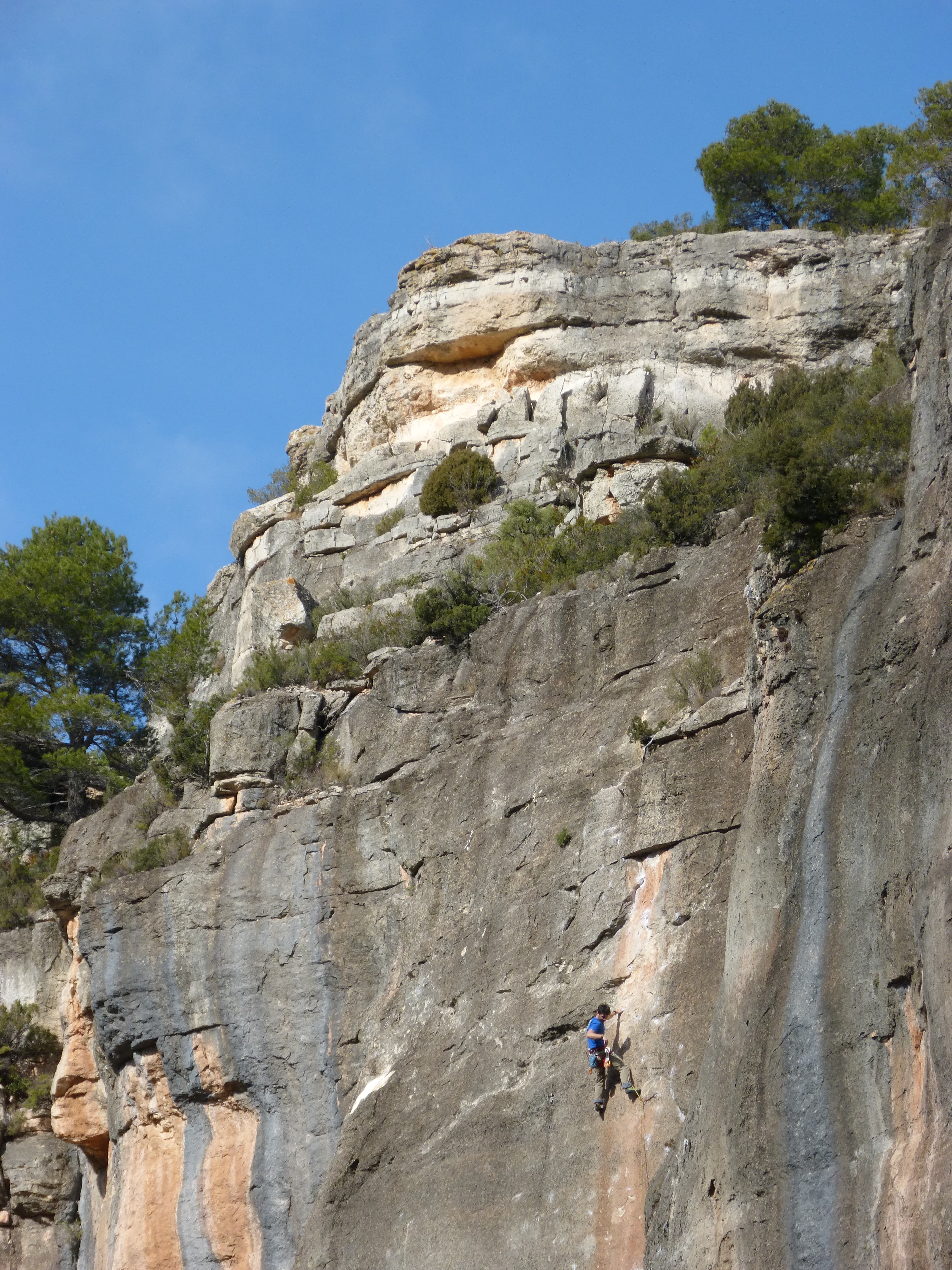 man wearing blue t-shirt climbing on rocky mountain under clear blue sky