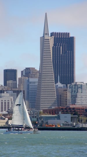white sail boat and gray cone shaped high rise building thumbnail