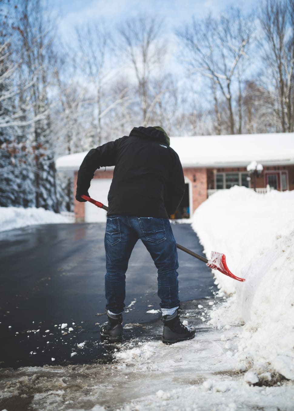 person in black jacket and blue denim pants wearing black boots holding snow shovel during daytime preview