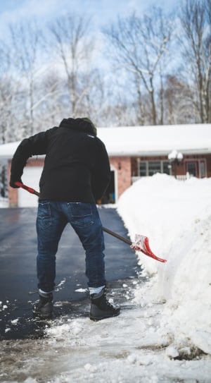person in black jacket and blue denim pants wearing black boots holding snow shovel during daytime thumbnail