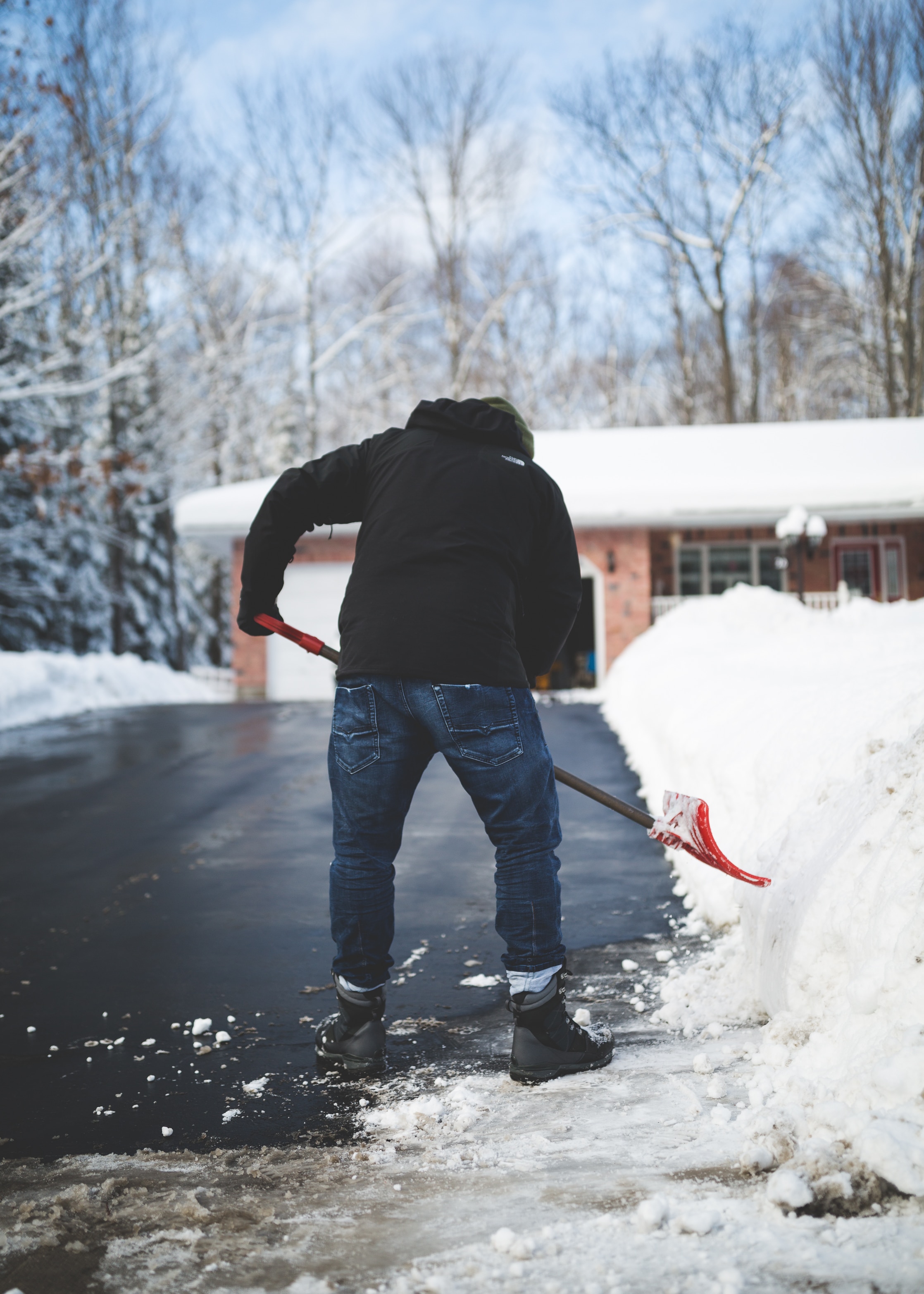 person in black jacket and blue denim pants wearing black boots holding snow shovel during daytime