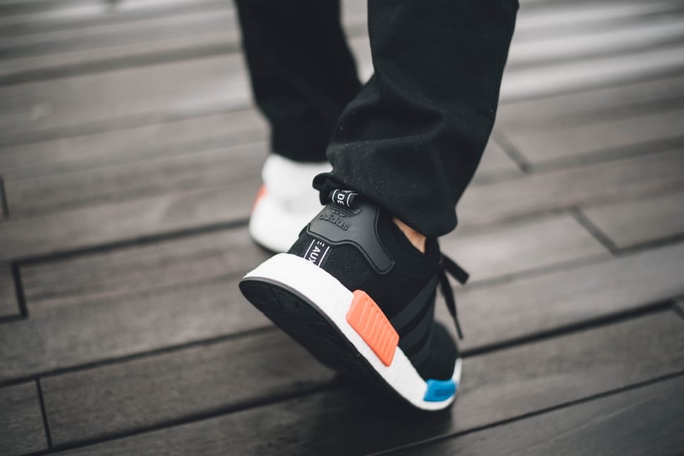 person wearing black pants and black-and-white adidas nmd walking on black parquet flooring preview