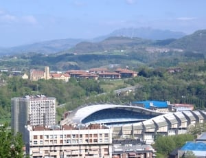 white and grey stadium structure surrounded with green trees thumbnail
