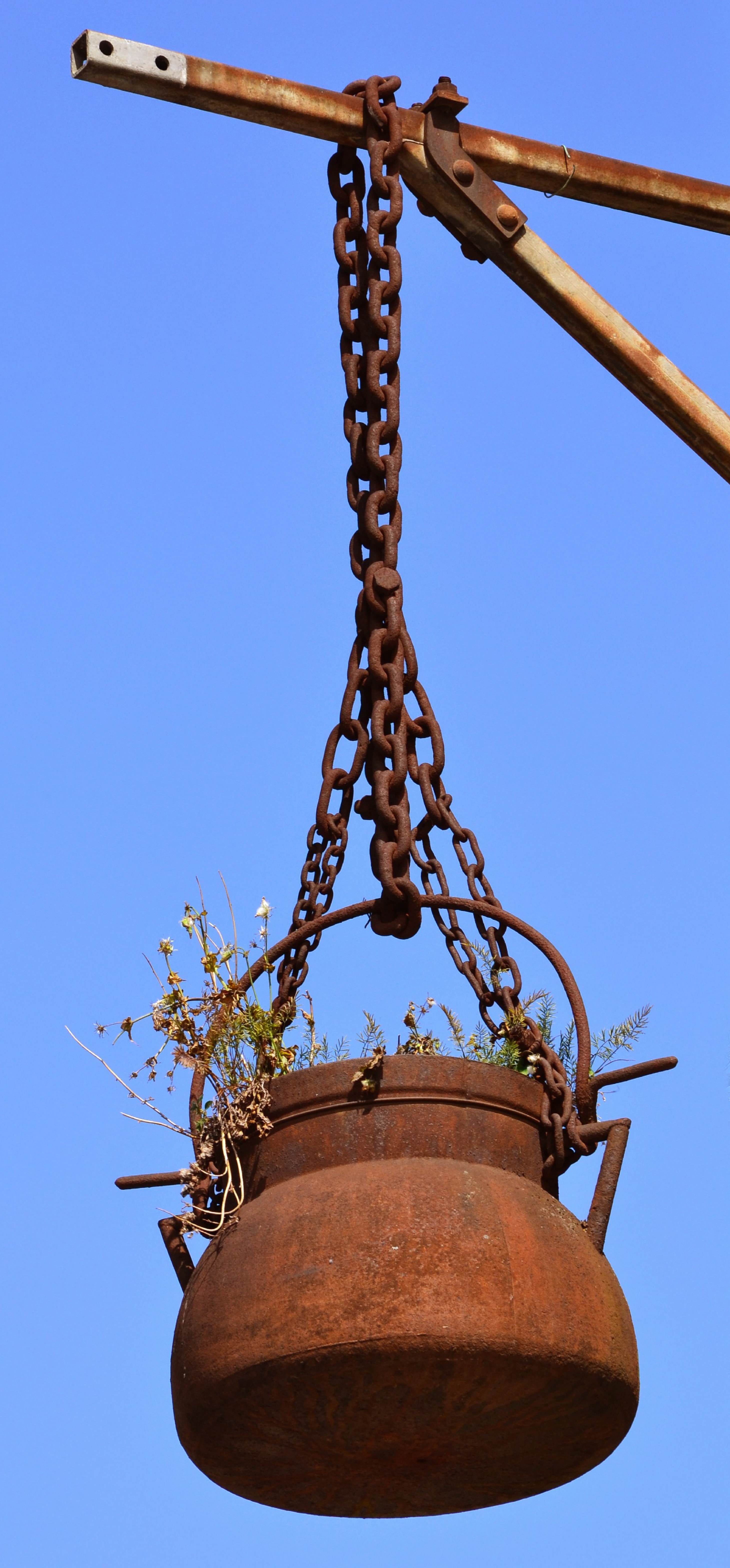 brown metal pot hanging on post with chains under blue sky during daytime