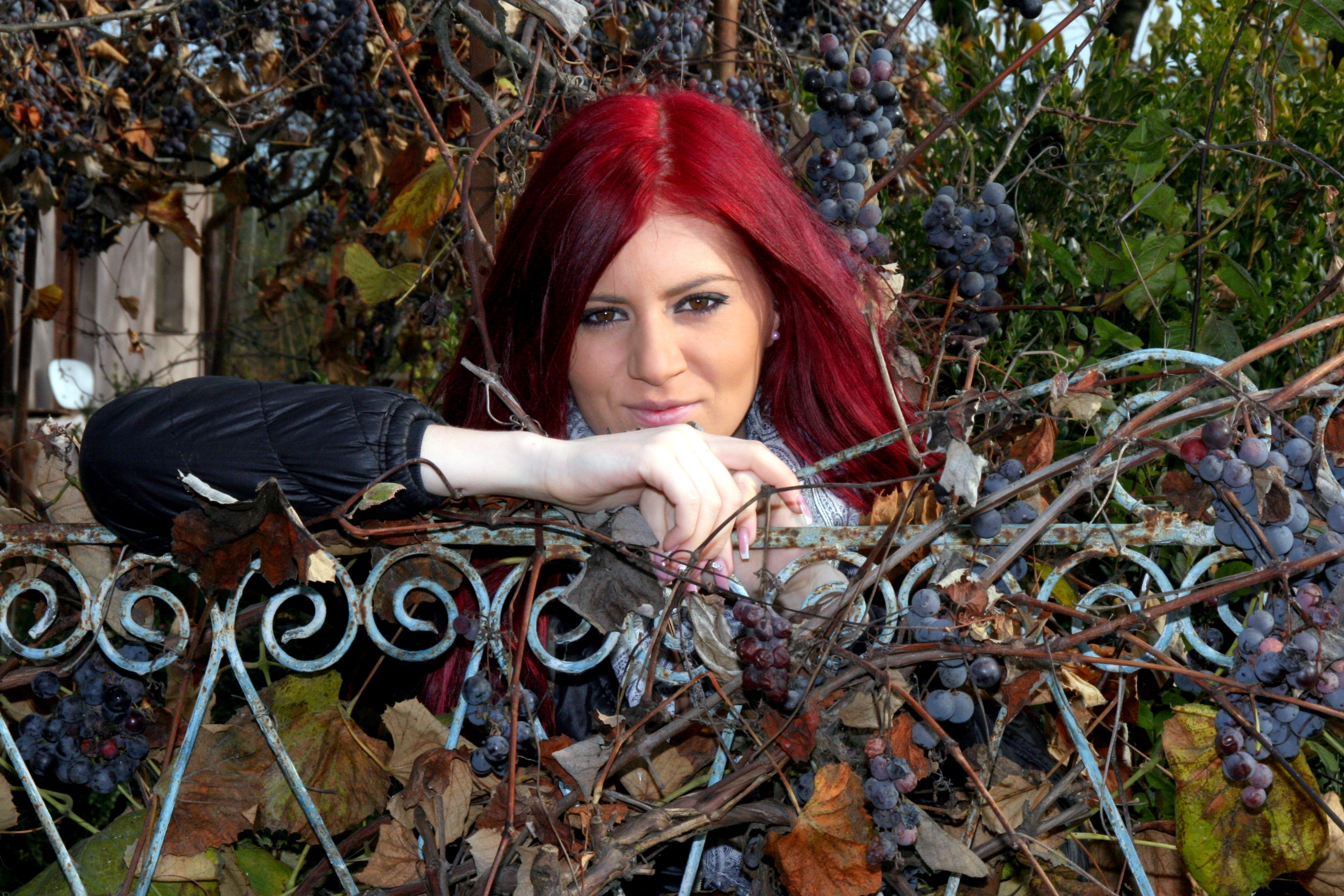 red haired woman leaning on steel fence with grape vines