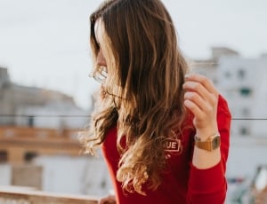 woman wearing red long sleeve top with gold watch standing outside at daytime thumbnail