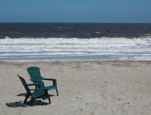 2 dark green plastic armchairs on gray sand near seashore thumbnail