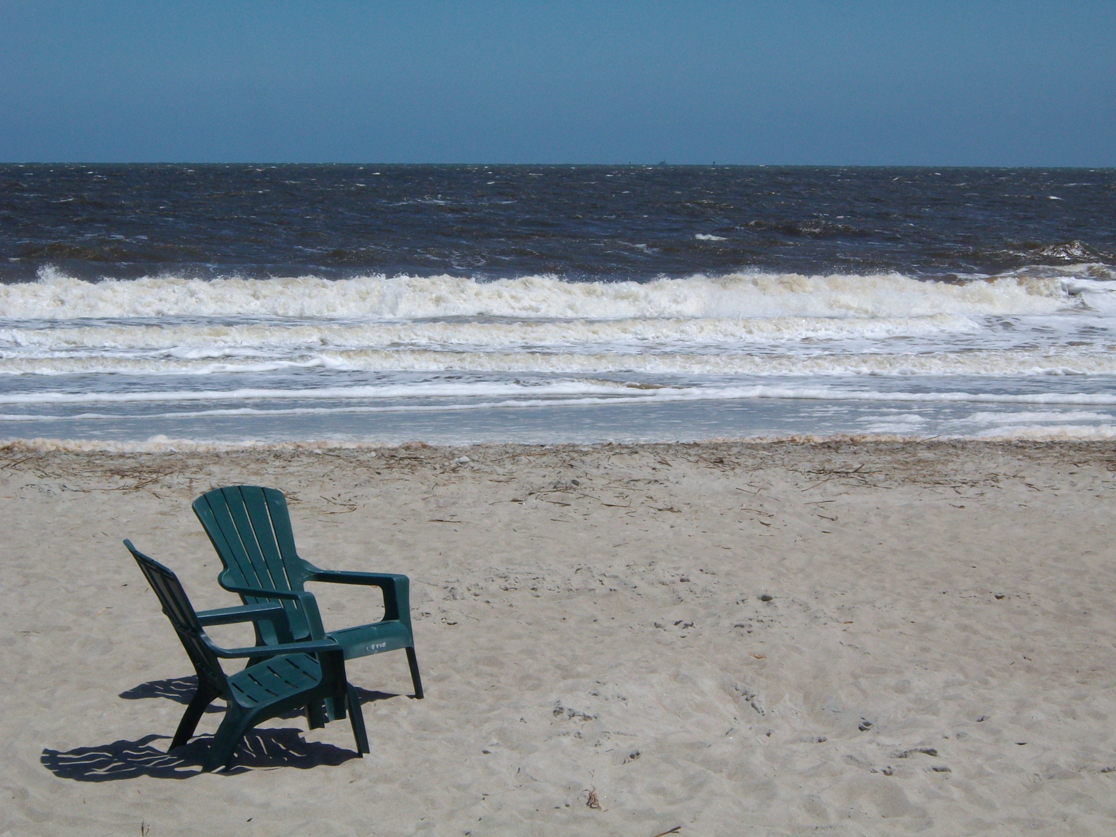 2 dark green plastic armchairs on gray sand near seashore