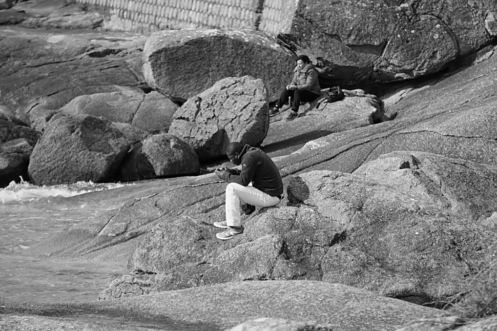 gray scale photo of man sitting on rock preview