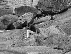 gray scale photo of man sitting on rock thumbnail