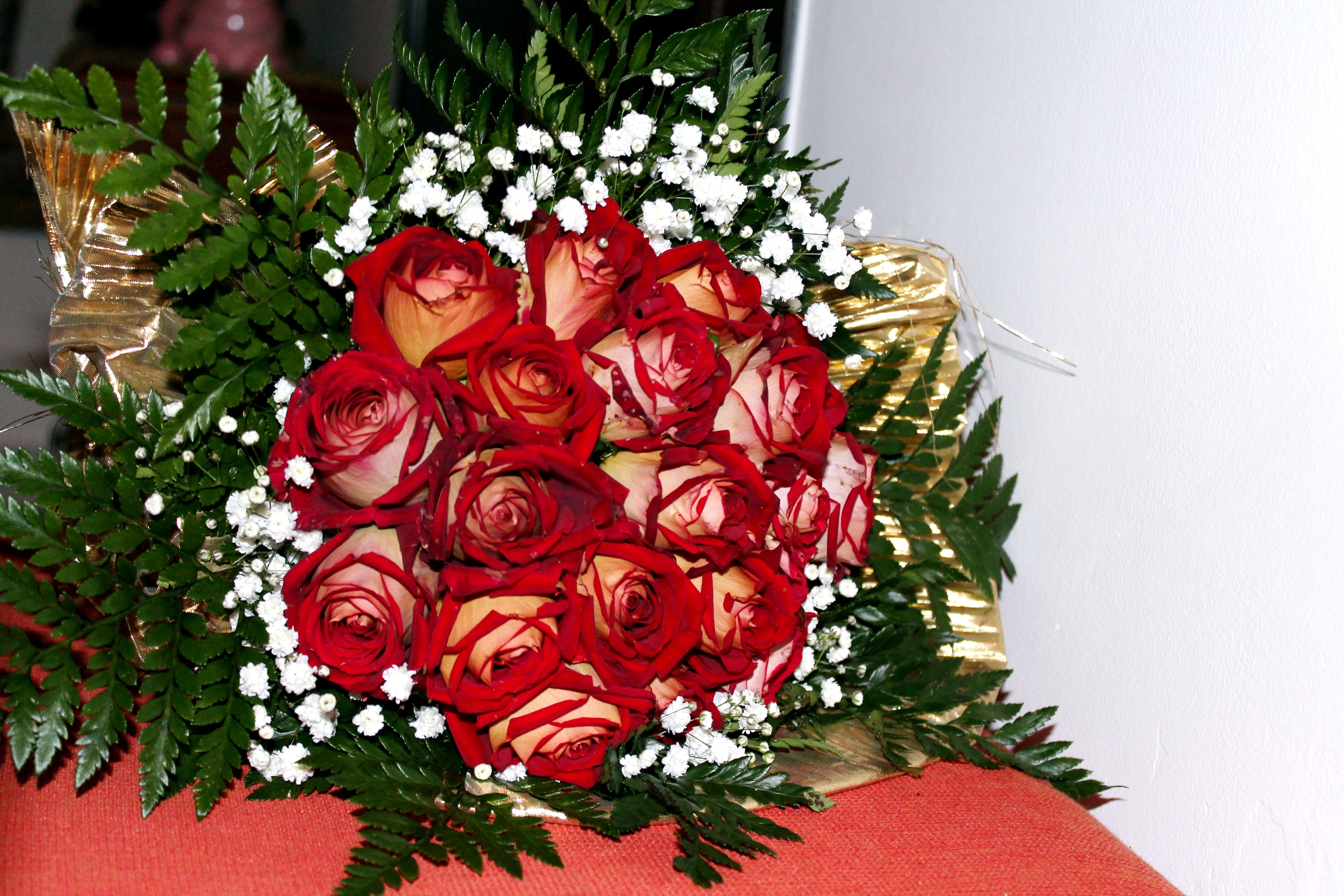 red and white roses surrounds with green fern plants of red textile
