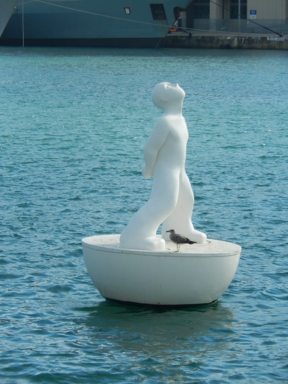 statue of man beside grey bird on body of water during daytime preview
