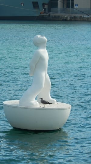 statue of man beside grey bird on body of water during daytime thumbnail