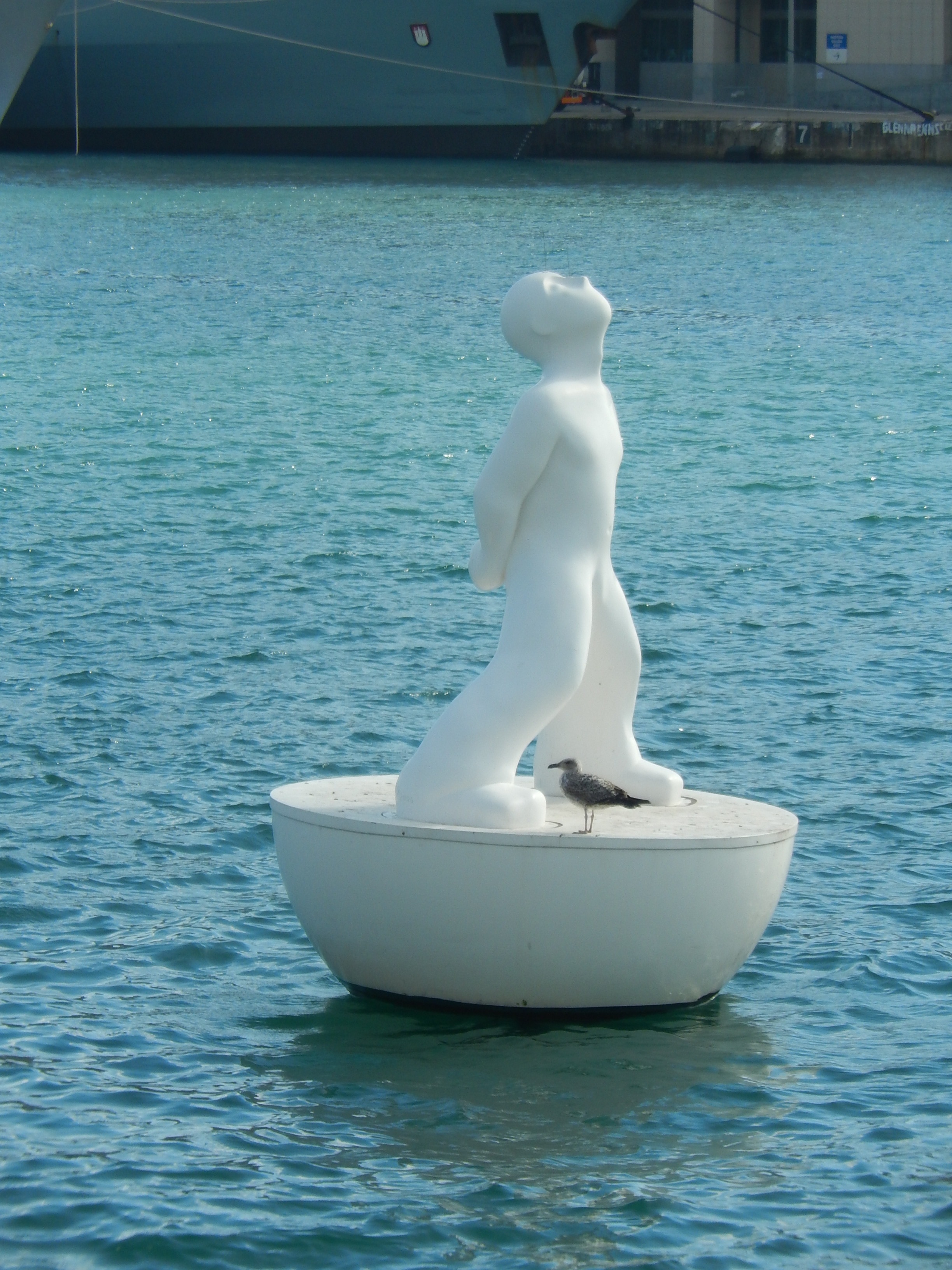 statue of man beside grey bird on body of water during daytime