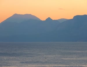 body of water near mountains during sunset thumbnail