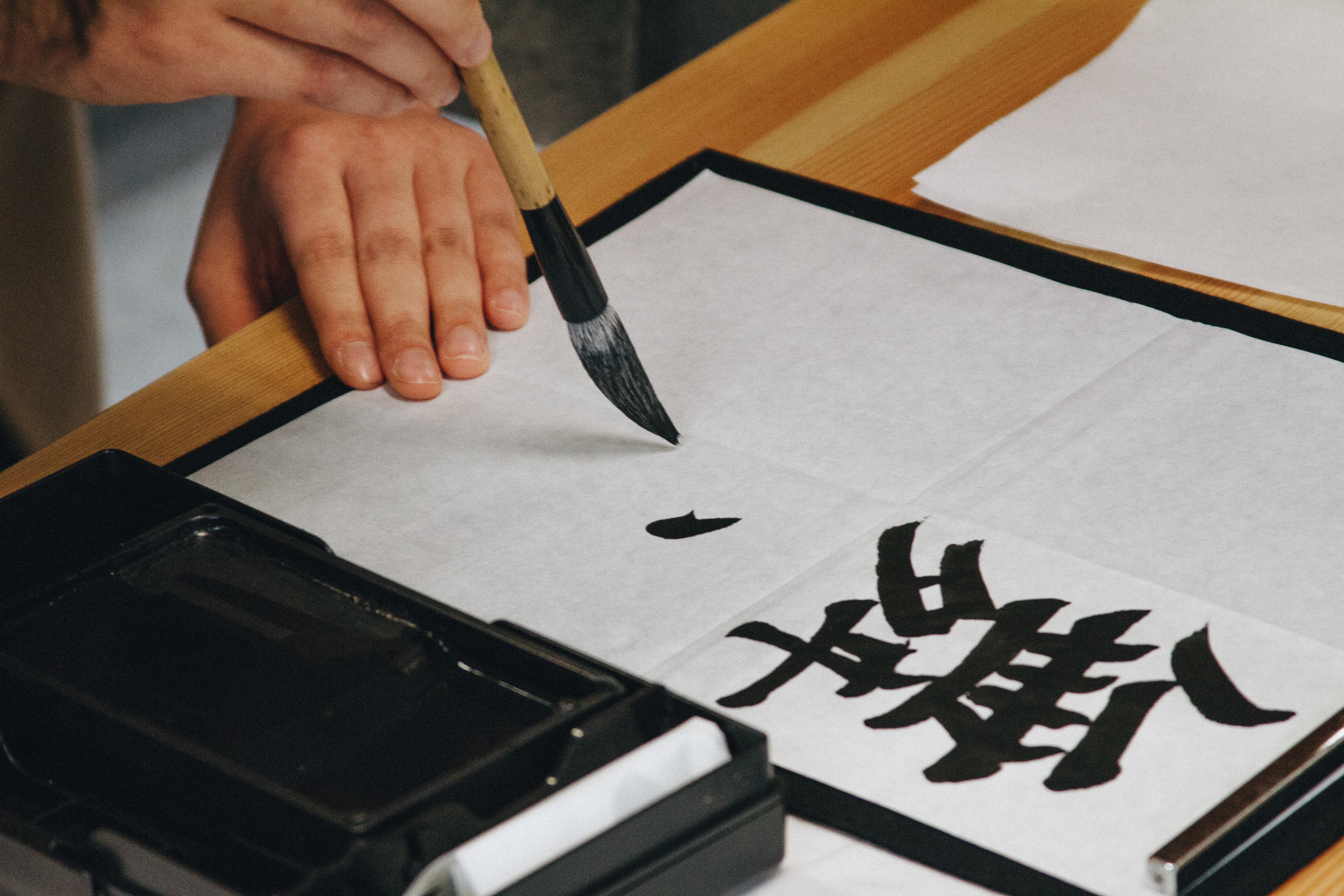 person holding paint brush writing kanji text