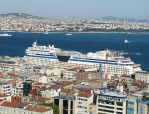 blue and white cruiseship on the body of water dock in brown and white houses thumbnail