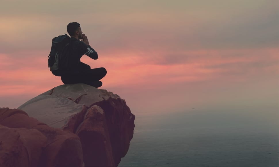 man in black shirt sitting on rock cliff during sunset preview