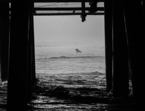 view from under the dock showing surfer in grayscale photography thumbnail