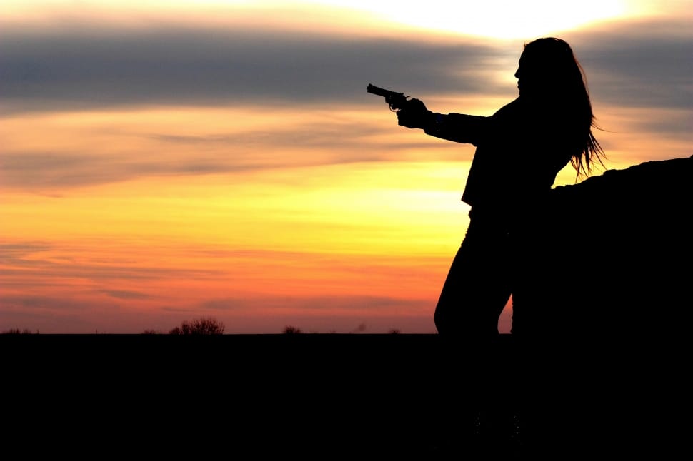 silhouette of woman holding revolver during golden hour preview