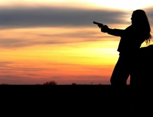 silhouette of woman holding revolver during golden hour thumbnail
